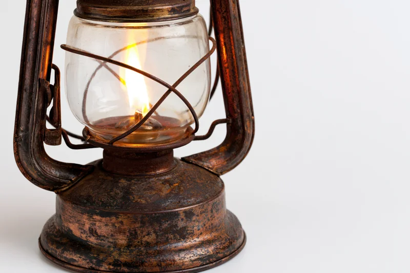 Antique kerosene lantern with lit flame glowing inside, isolated on white background