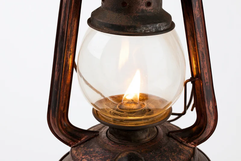 Close-up of a lit antique kerosene lantern with glowing flame inside glass globe on white background
