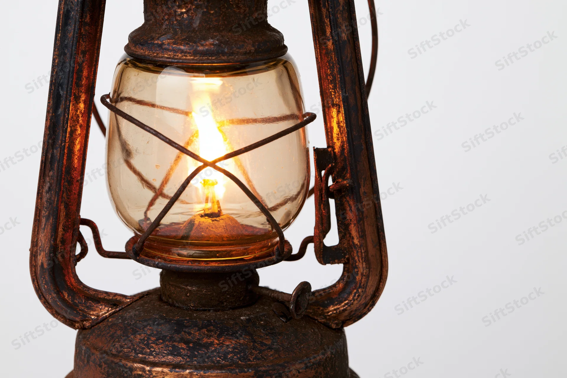 Antique kerosene lantern with lit flame glowing inside glass enclosure on white background
