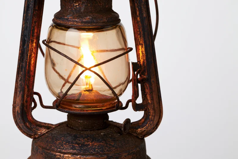 Antique kerosene lantern with lit flame glowing inside glass enclosure on white background