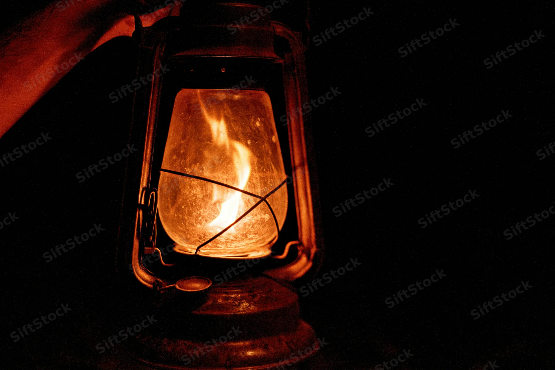 Hand holding a glowing vintage kerosene lantern in the dark