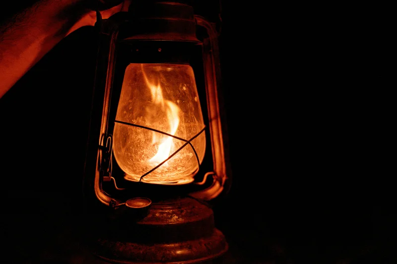 Hand holding a glowing vintage kerosene lantern in the dark