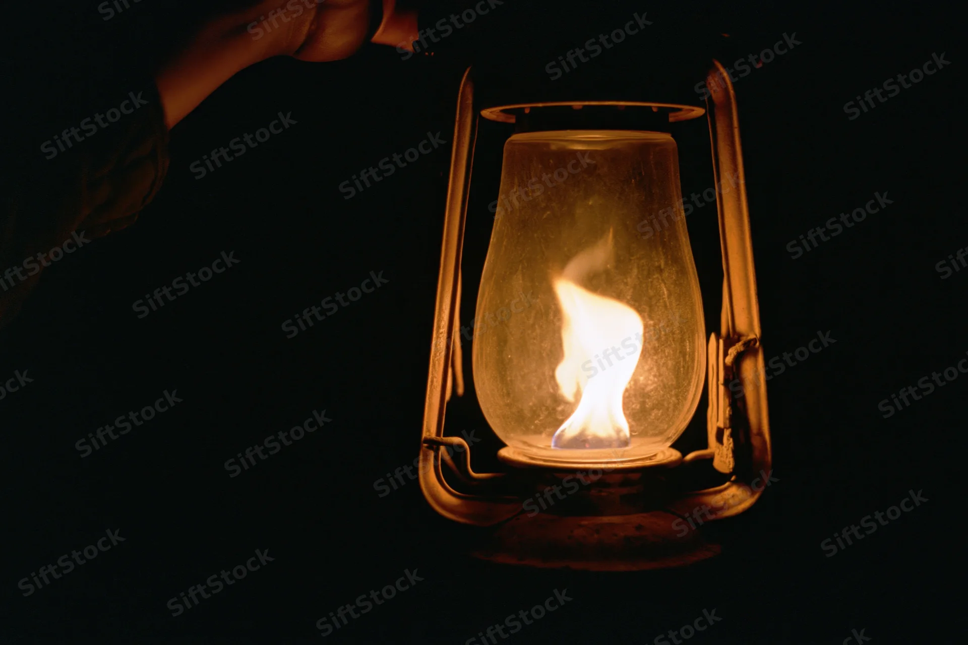 Hand holding a lit vintage kerosene lantern in the dark