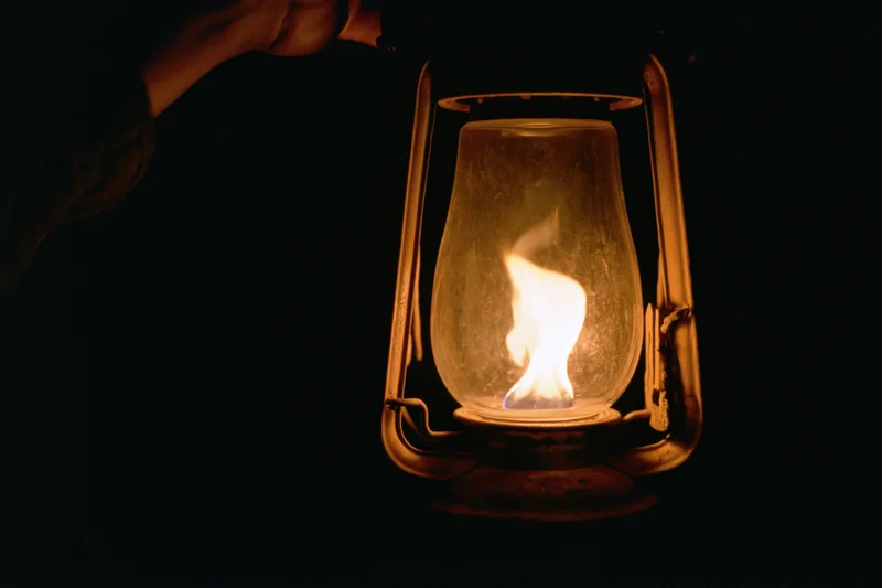 Hand holding a lit vintage kerosene lantern in the dark