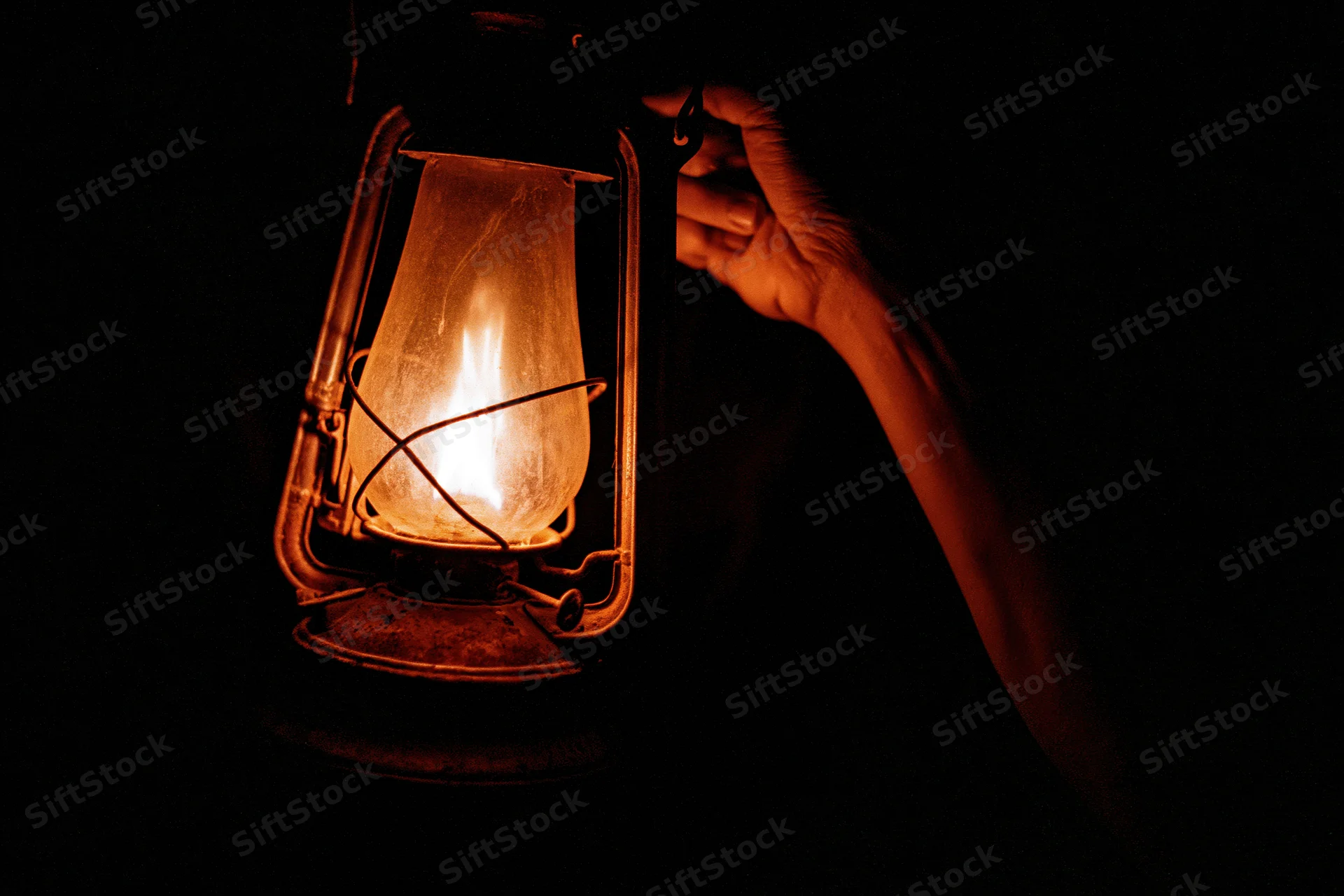 Hand holding an old kerosene lantern glowing in the dark