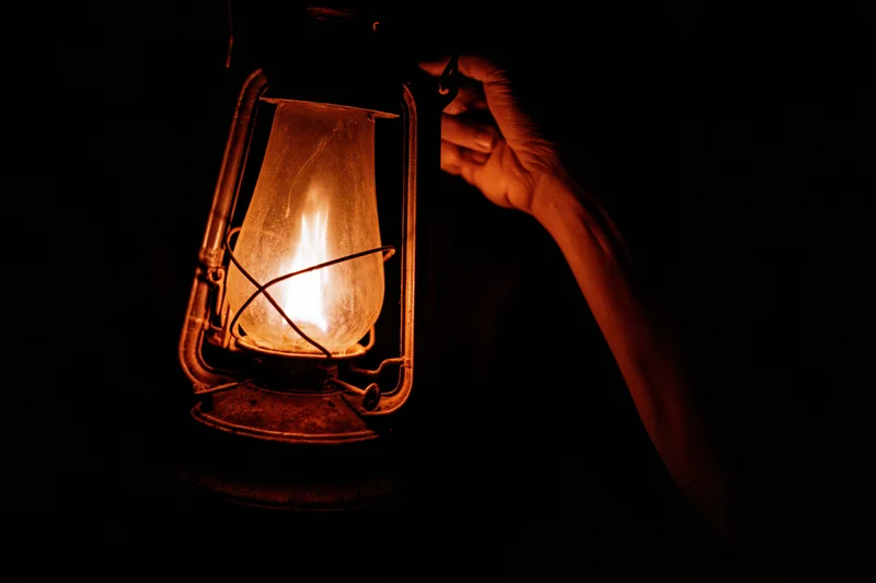 Hand holding an old kerosene lantern glowing in the dark