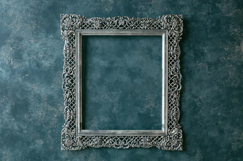 Ornate silver antique frame with intricate floral patterns mounted on dark textured wall