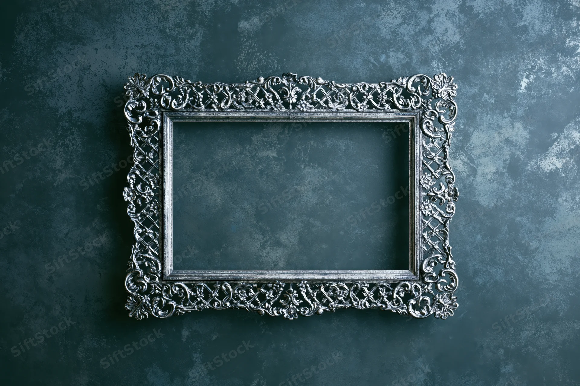 Ornate silver antique frame with intricate floral scrollwork hanging on a dark textured blue wall