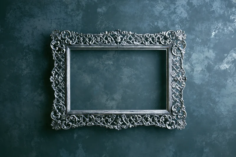 Ornate silver antique frame with intricate floral scrollwork hanging on a dark textured blue wall