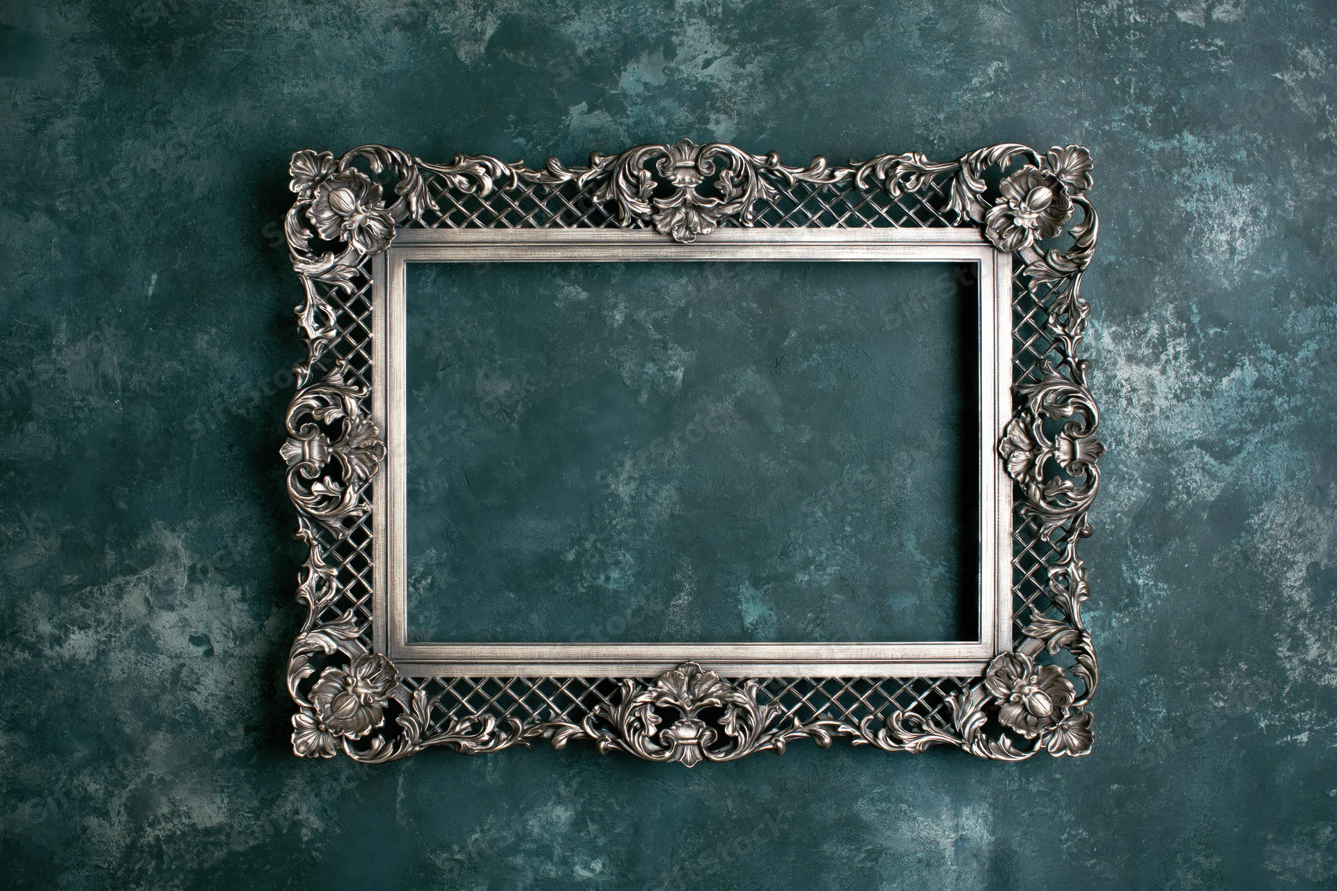 Ornate silver picture frame with floral and lattice details mounted on a textured teal wall