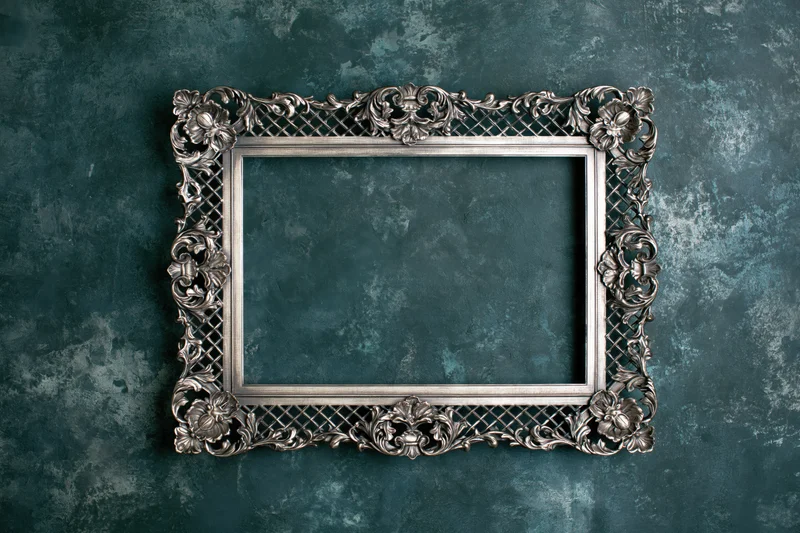 Ornate silver picture frame with floral and lattice details mounted on a textured teal wall