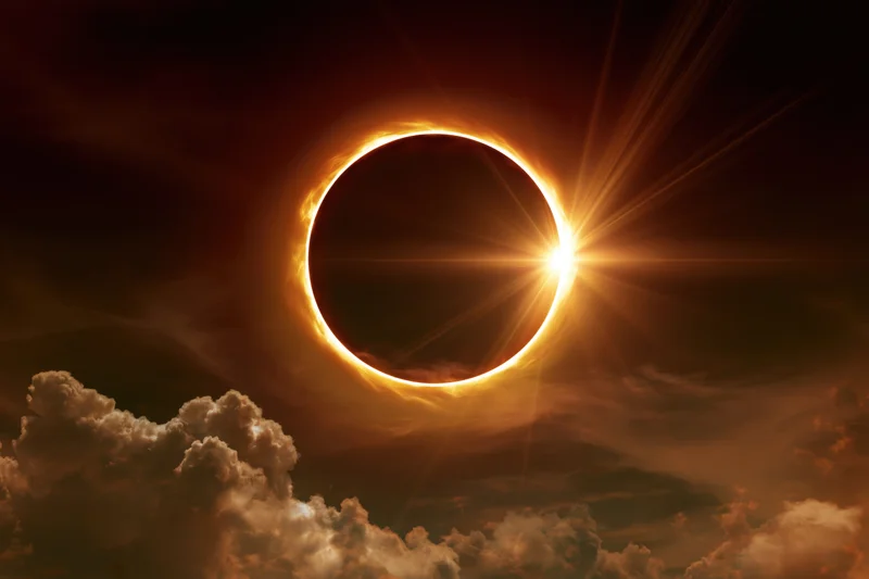 Annular solar eclipse at peak totality with moon centered and corona glowing against cloudy sky