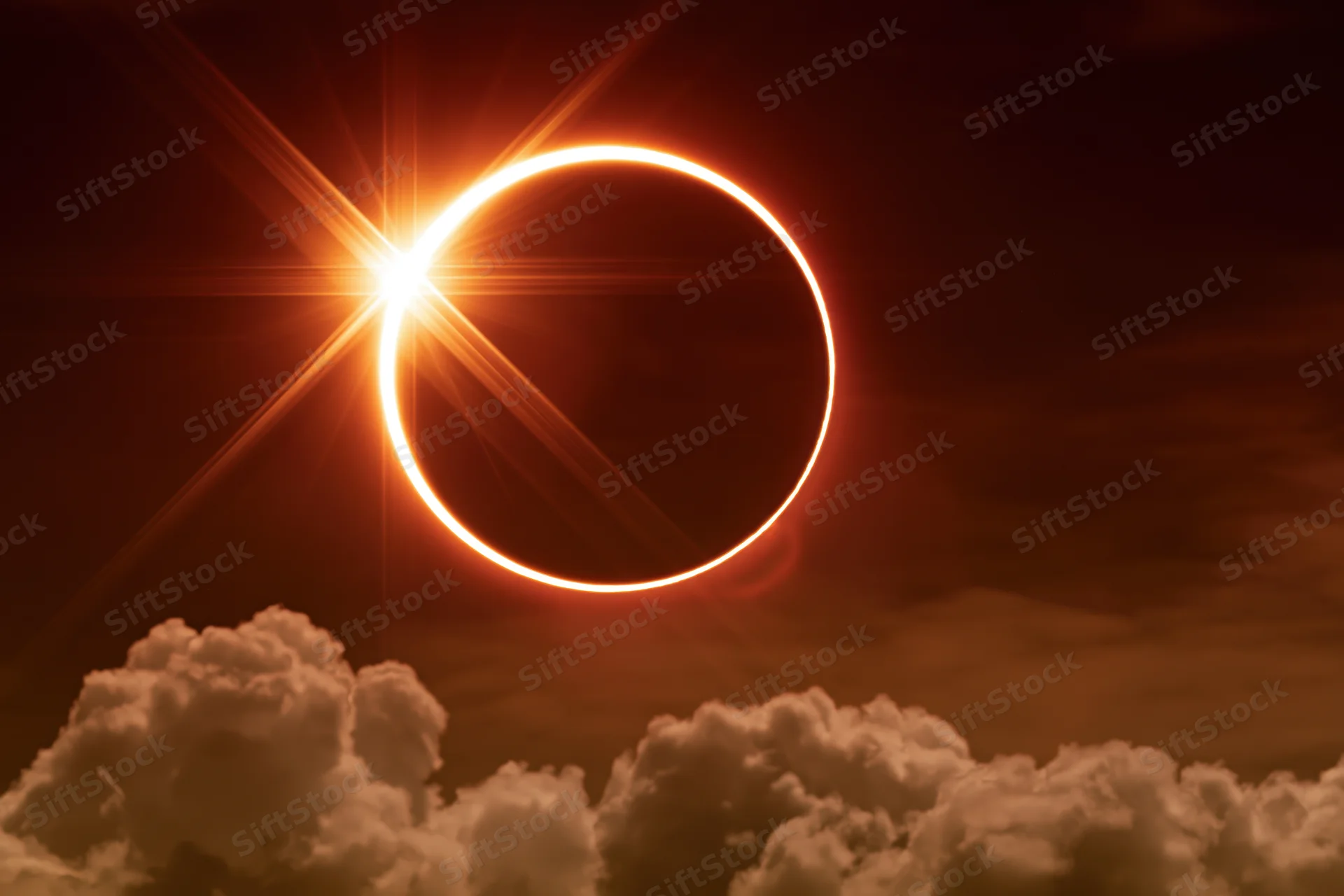 Annular solar eclipse at peak totality with moon centered in sun's disk above clouds