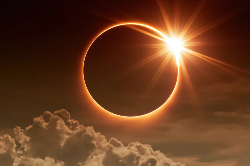 Annular solar eclipse with moon centered in sky above clouds