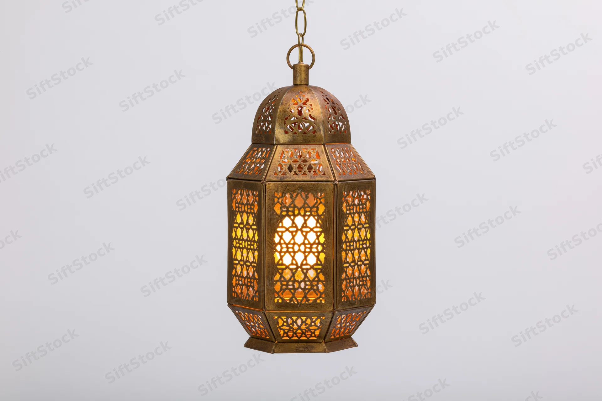Antique moroccan brass lantern hanging from chain with intricate geometric cutouts glowing warmly