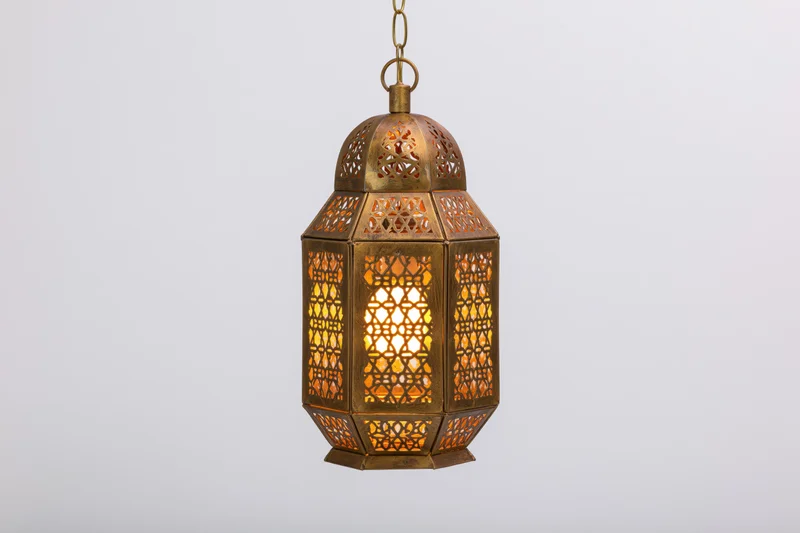 Antique moroccan brass lantern hanging from chain with intricate geometric cutouts glowing warmly