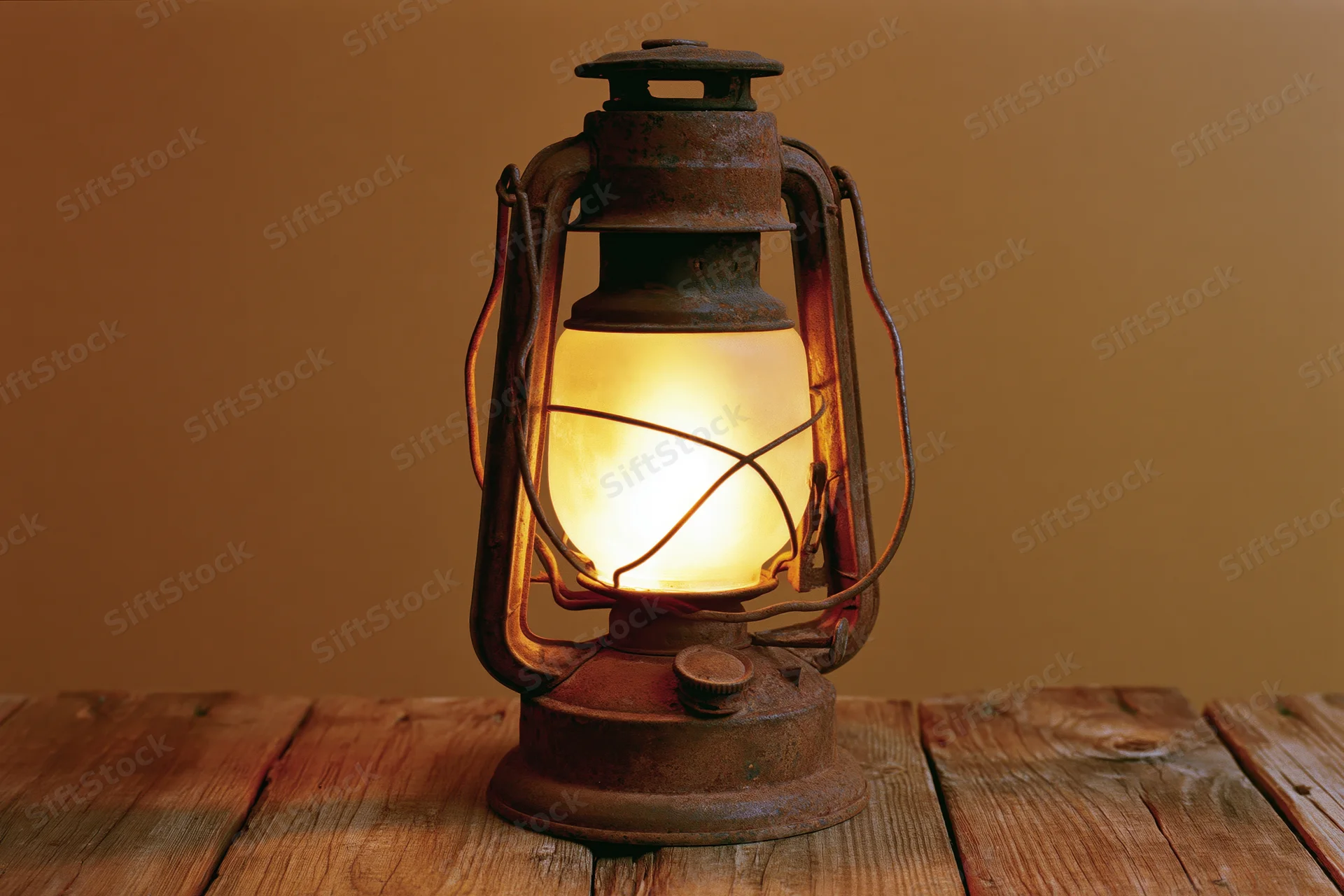 Antique rusty kerosene lantern glowing with warm amber flame on wooden table