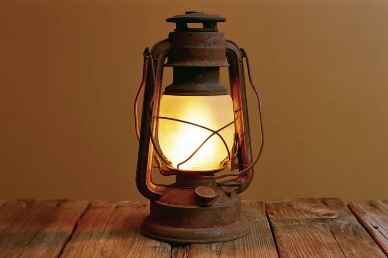 Antique rusty kerosene lantern glowing with warm amber flame on wooden table
