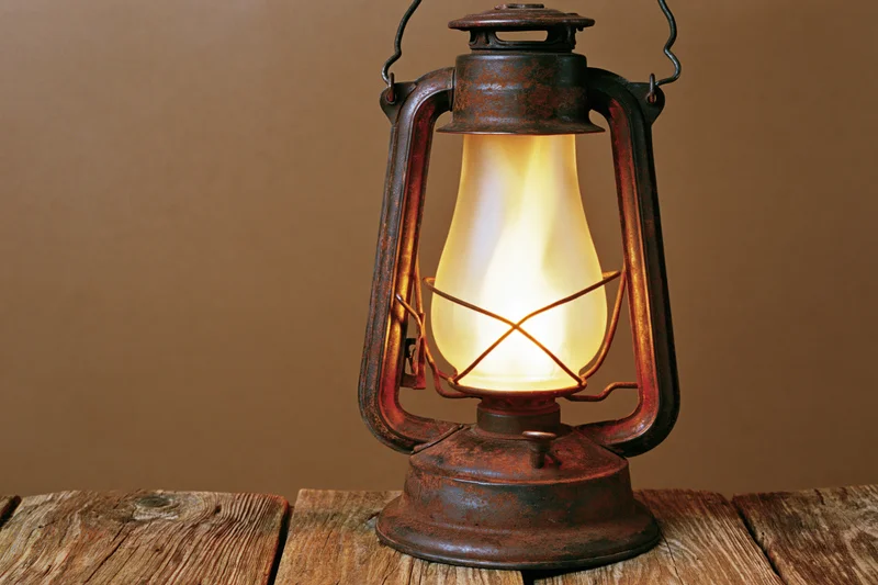 Antique rusty kerosene lantern glowing with warm amber flame on wooden surface