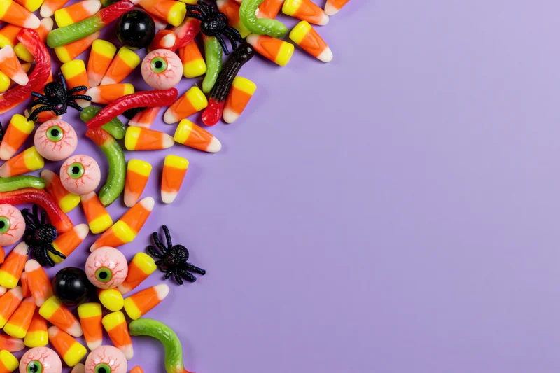 Assorted halloween candy scattered along left edge on purple background with copyspace