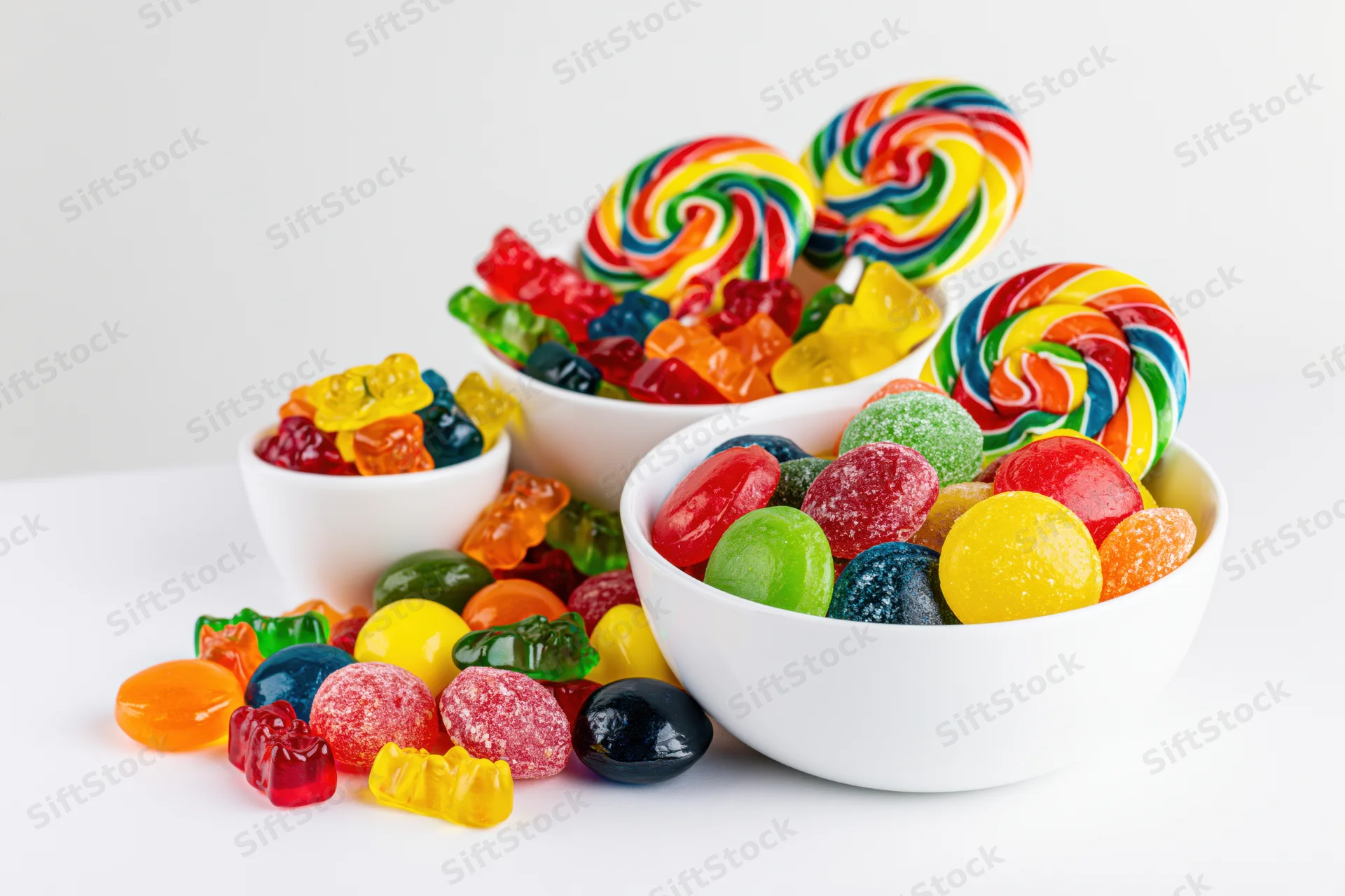 Assorted colorful candies in white ceramic bowls on a white surface