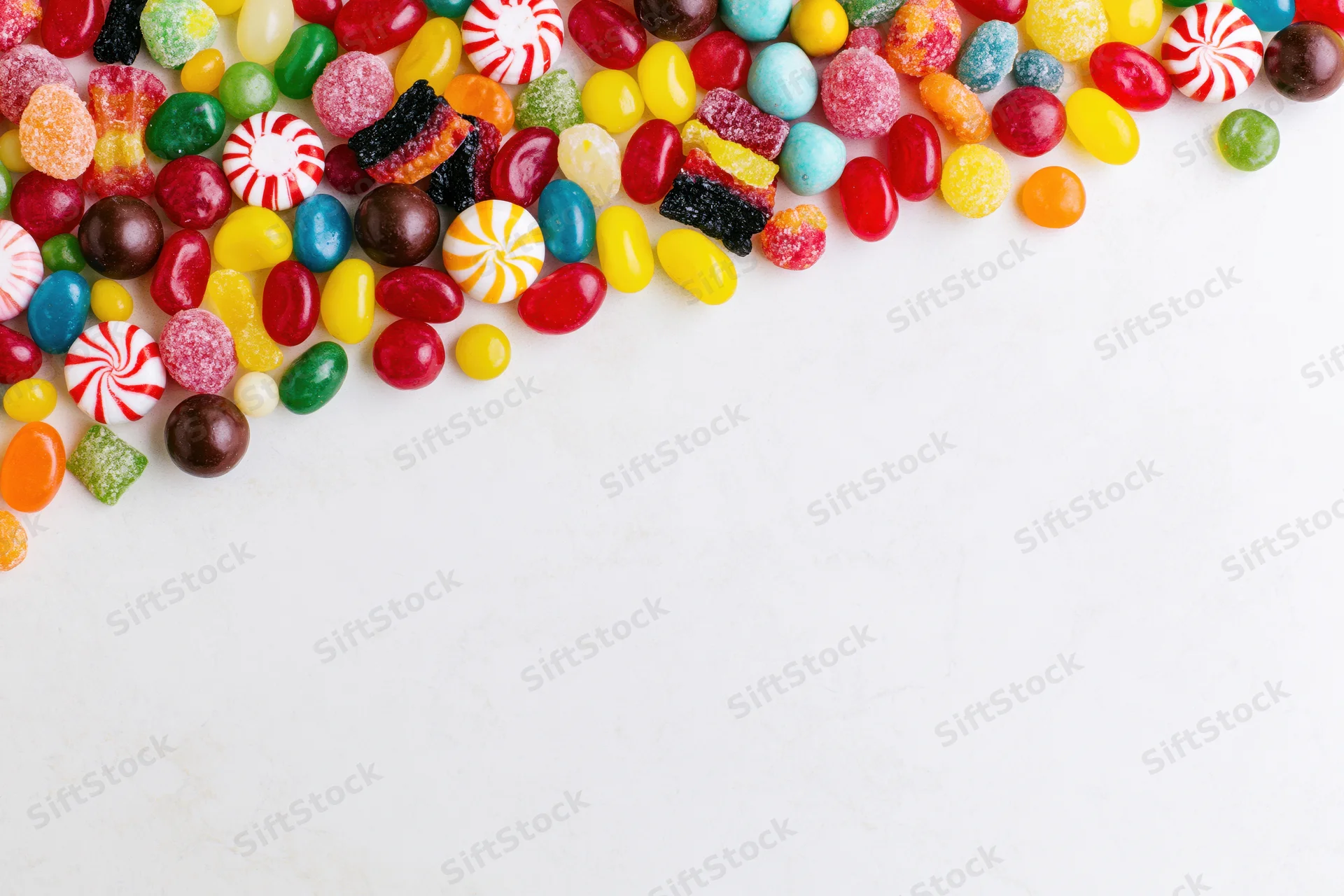 Assorted candies scattered across white surface with copyspace