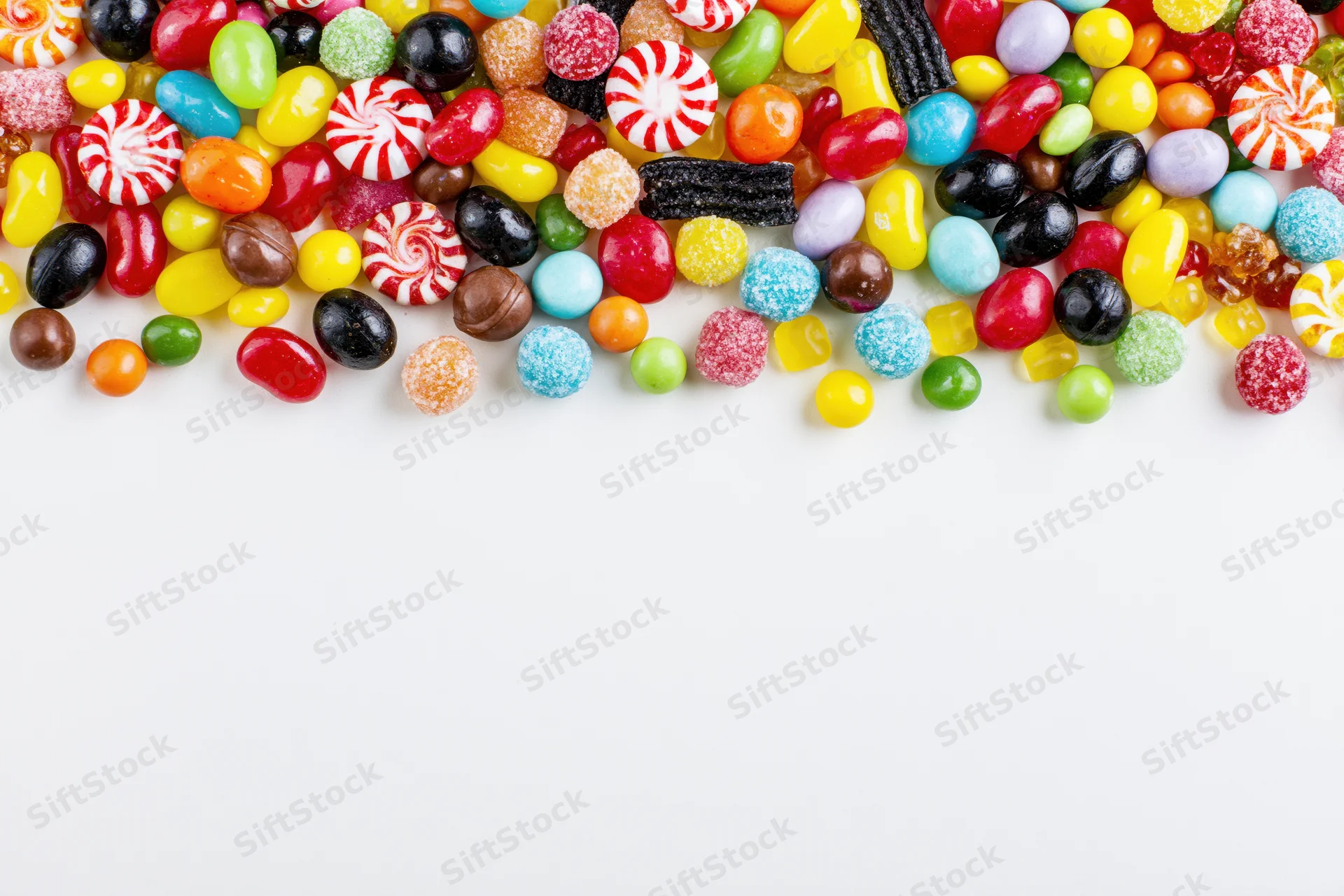 Assorted candies scattered across white surface with copyspace below