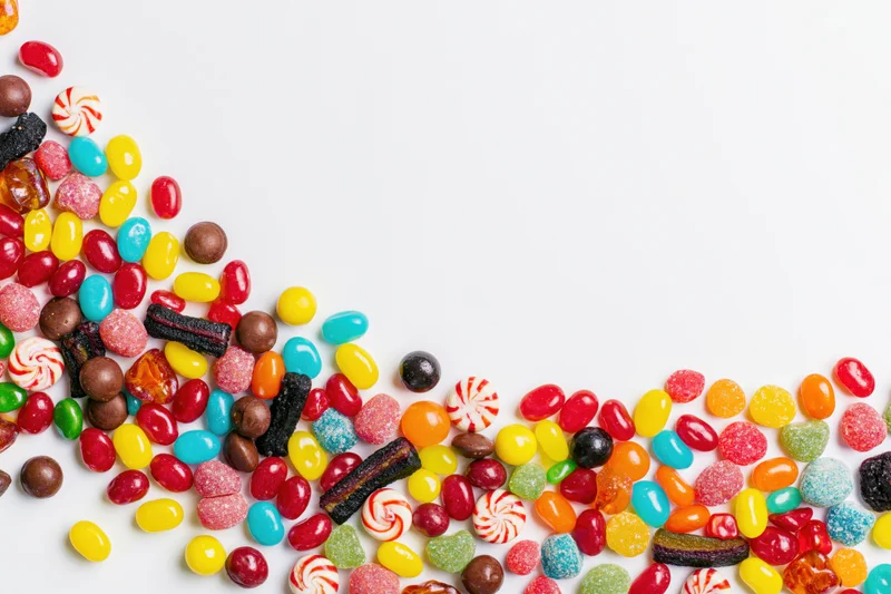 Assorted candies scattered across white surface with copyspace