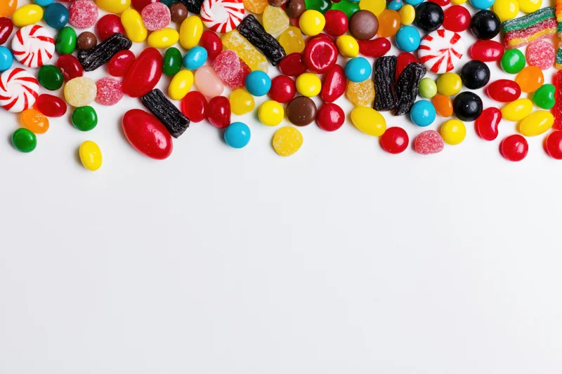 Assorted candies scattered across white surface with copyspace below