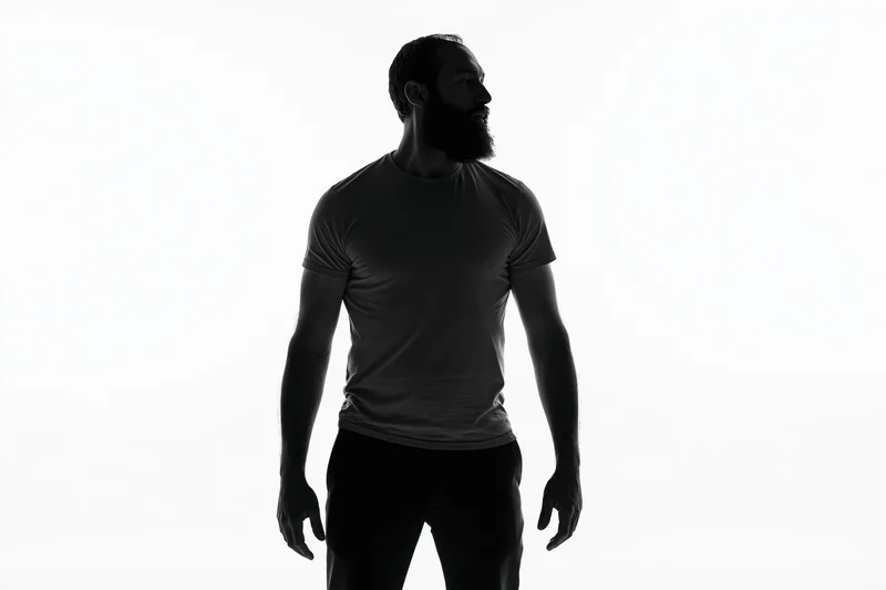 Bearded man standing in profile wearing a tshirt against a white background