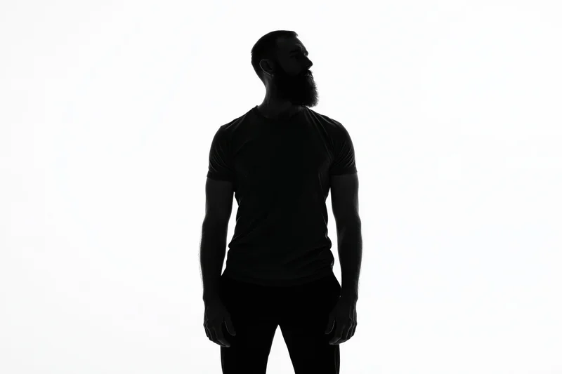 Bearded man standing in profile with hands at sides against white background