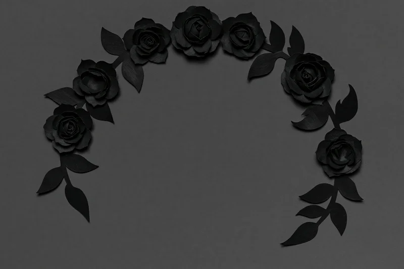 Black paper-cut roses and leaves arranged in a crescent wreath on dark surface