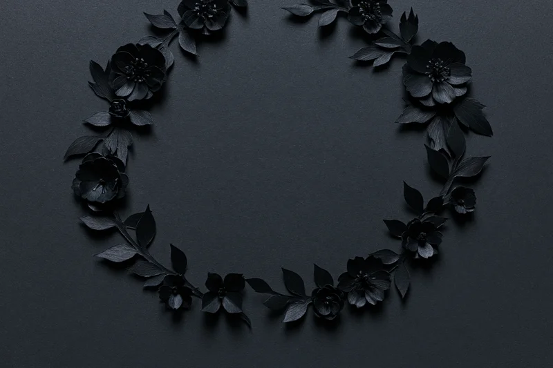 Black paper-cut flowers and leaves arranged in a crescent wreath on dark surface