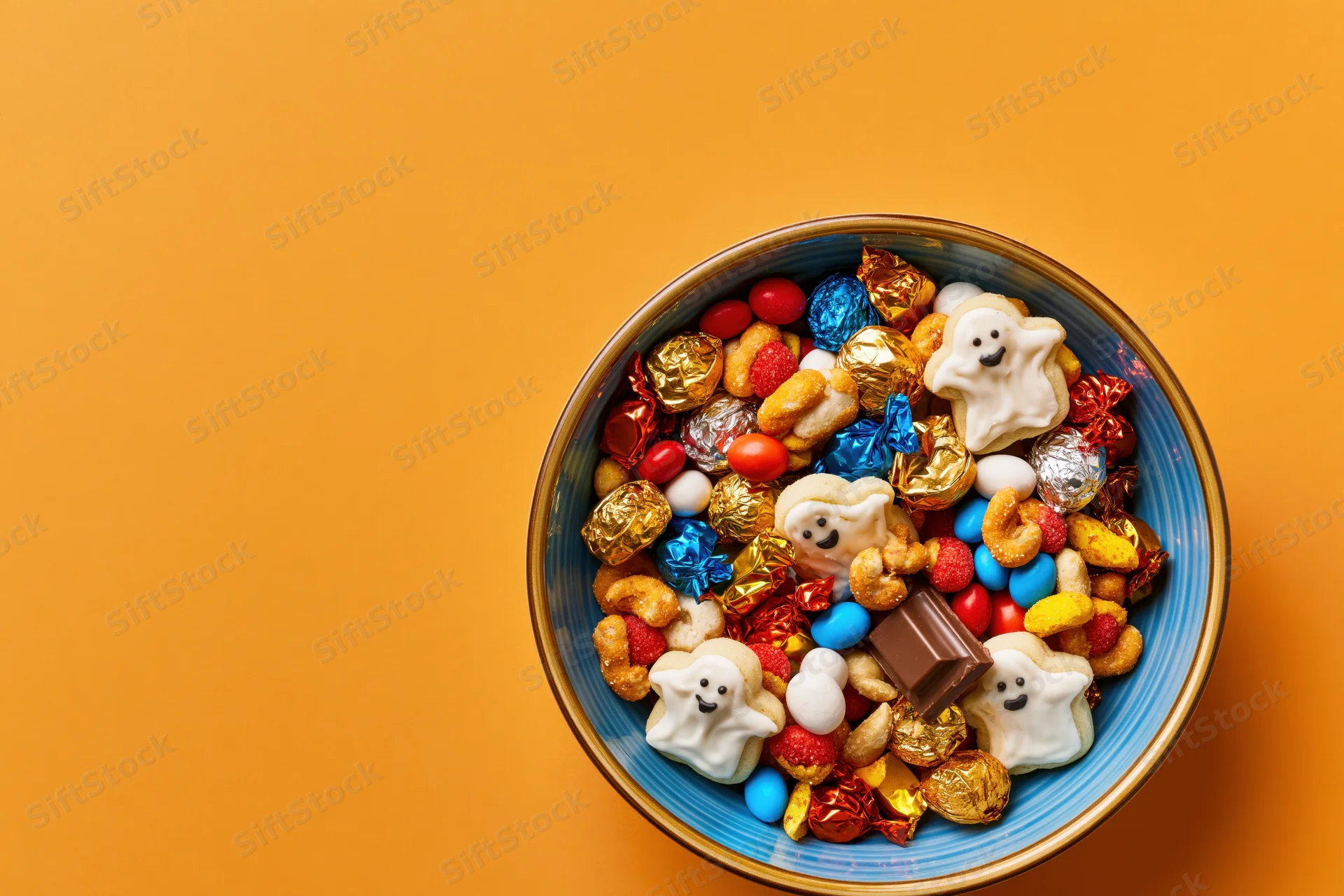 Blue ceramic bowl filled with halloween candy and ghost-shaped marshmallows on orange background