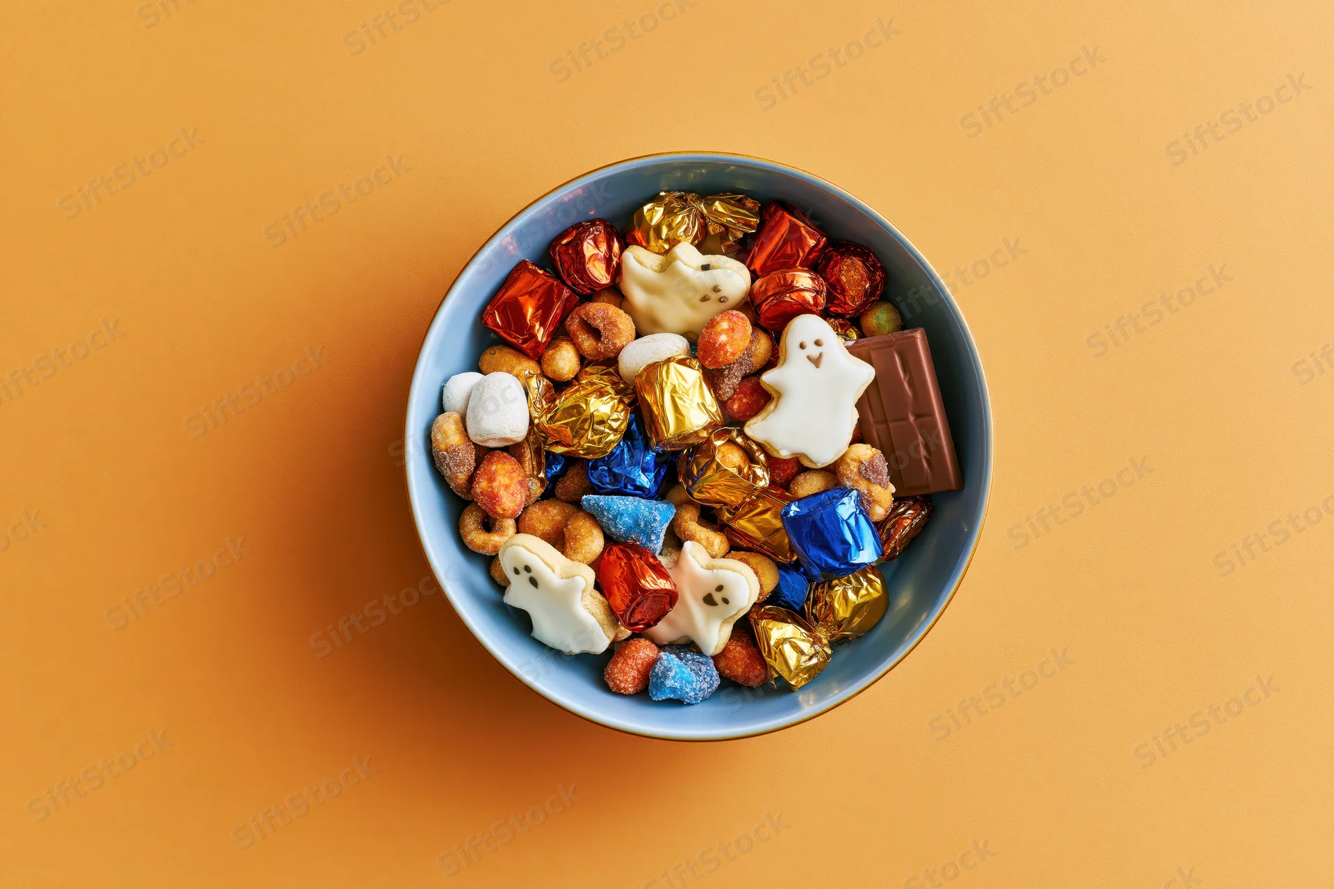 Blue ceramic bowl filled with halloween candy and ghost-shaped sweets on orange background