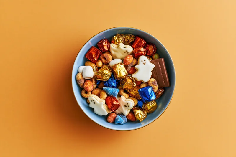 Blue ceramic bowl filled with halloween candy and ghost-shaped sweets on orange background