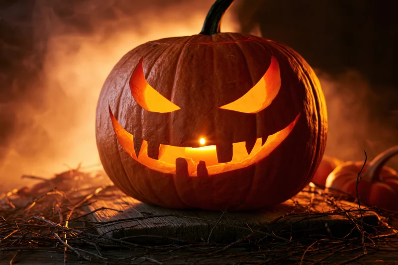 Carved pumpkin glowing from within on wooden surface surrounded by twigs and smoke