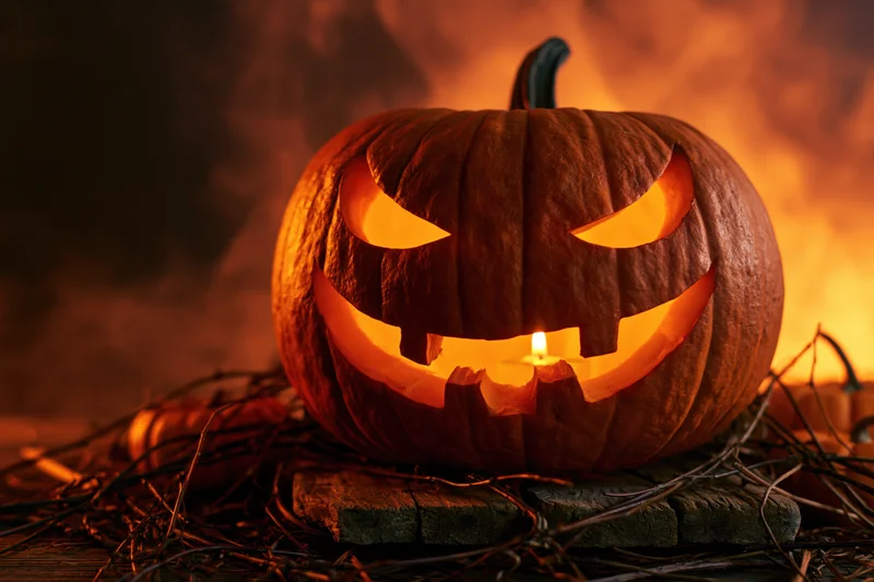Carved pumpkin glowing from within on wooden surface surrounded by twigs and smoke