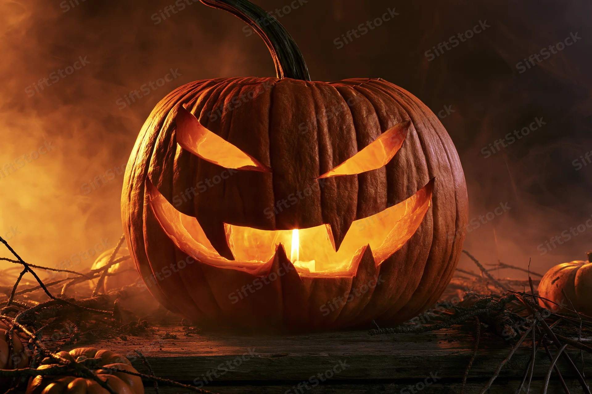 Carved pumpkin glowing from within on a dark smoky background with branches and smaller pumpkins around