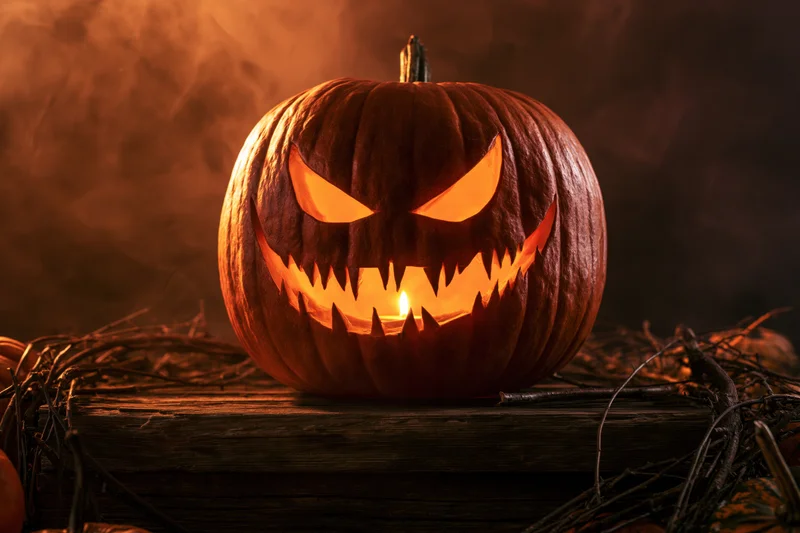 Carved pumpkin with glowing face on wooden table surrounded by twigs and smoke