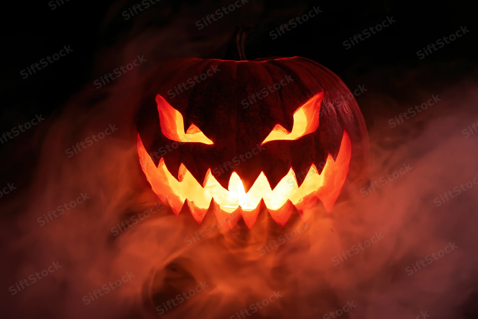 Carved jack-o-lantern with jagged teeth glowing in smoke at night