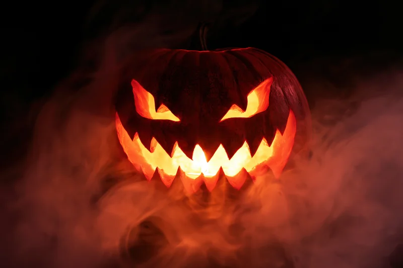 Carved jack-o-lantern with jagged teeth glowing in smoke at night