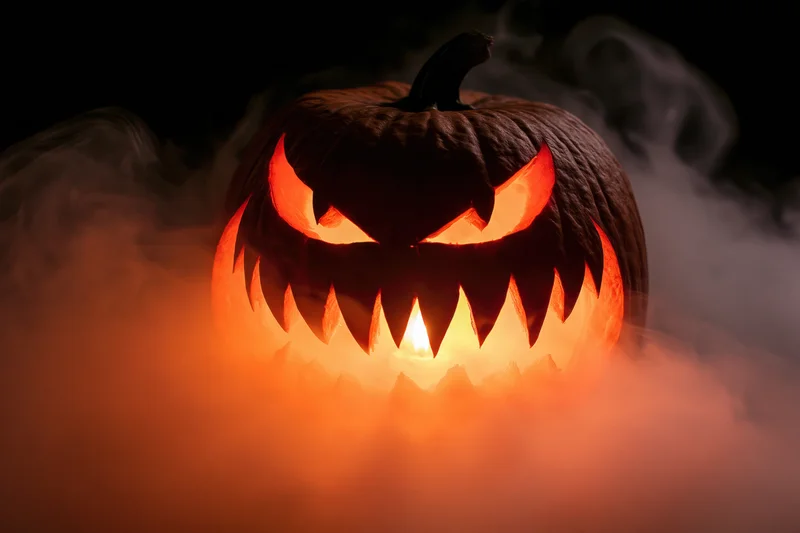 Carved jack-o-lantern glowing with jagged teeth in dark smoke at night