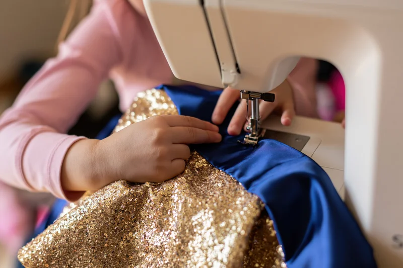 Child guiding gold glitter and blue fabric under sewing machine needle