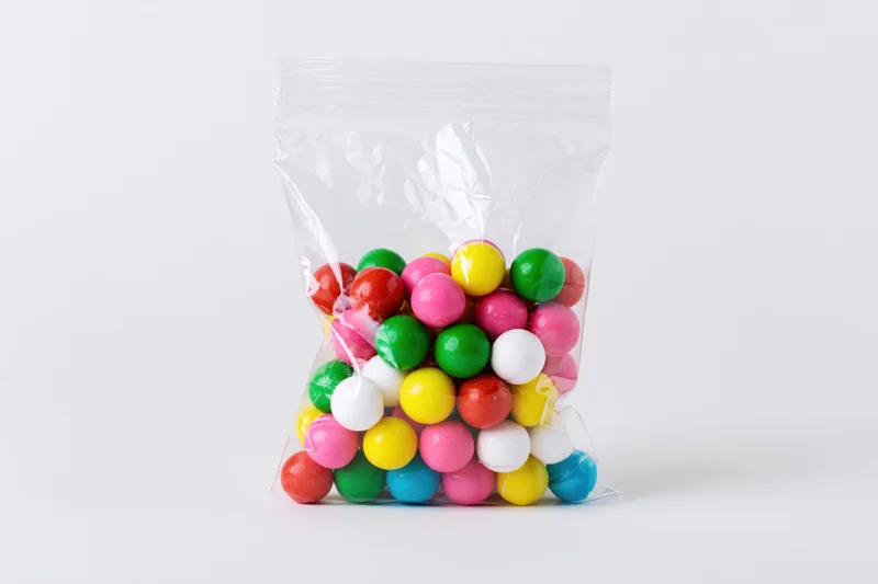 Clear plastic bag filled with colorful round gumballs on white background
