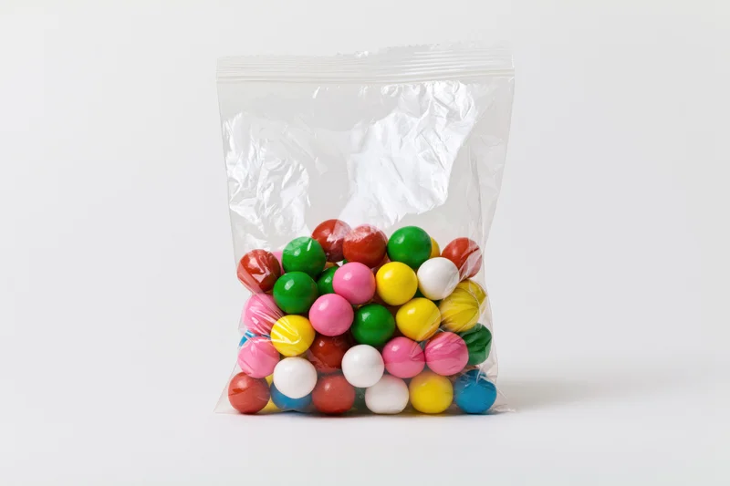Clear plastic bag filled with colorful gumballs on white background