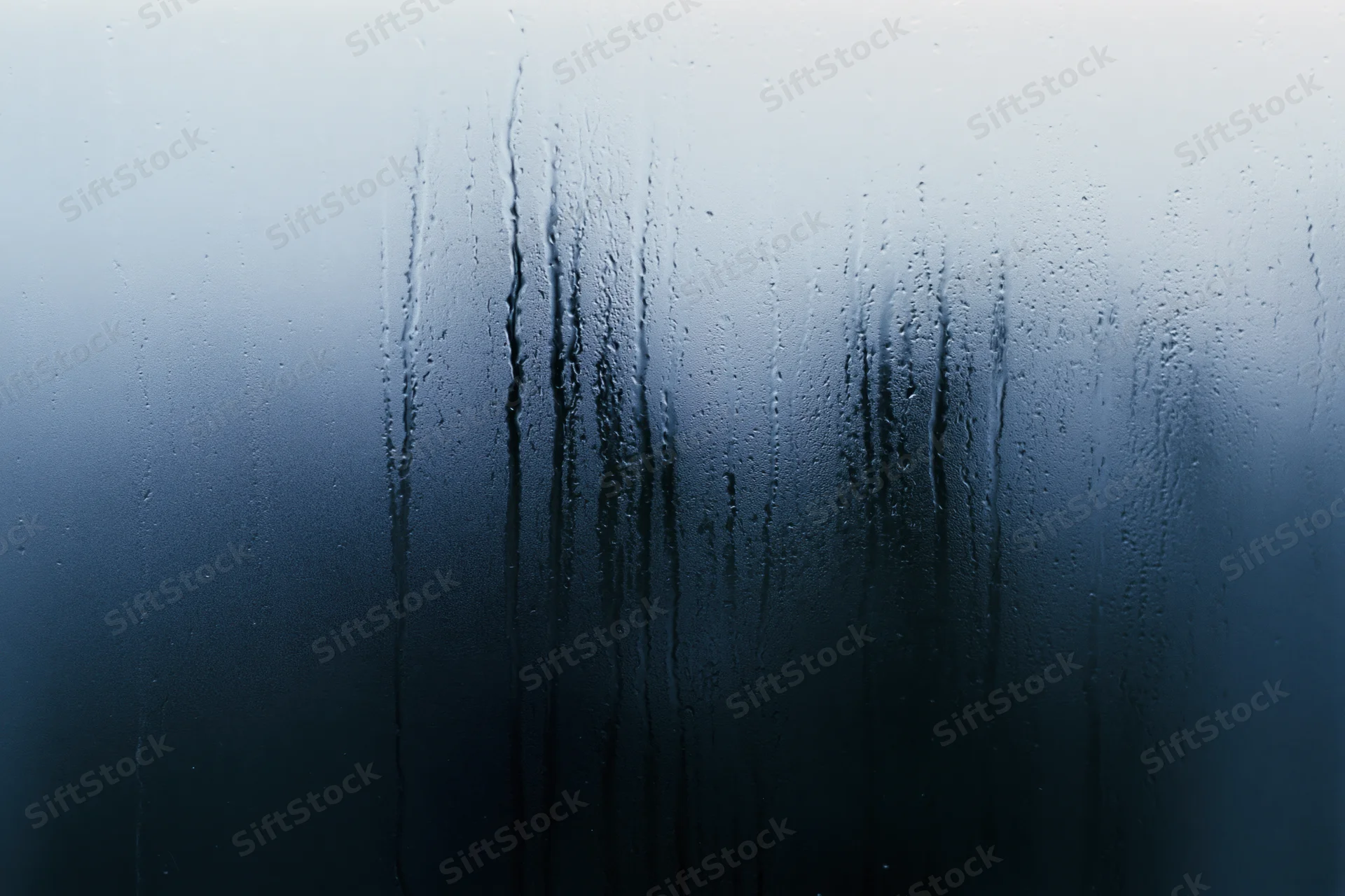Close-up of rain-streaked and fogged window glass with water droplets and condensation