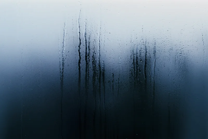 Close-up of rain-streaked and fogged window glass with water droplets and condensation