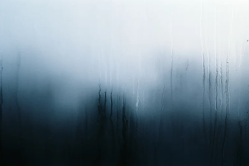 Close-up of rain-streaked and fogged window glass with water droplets and condensation