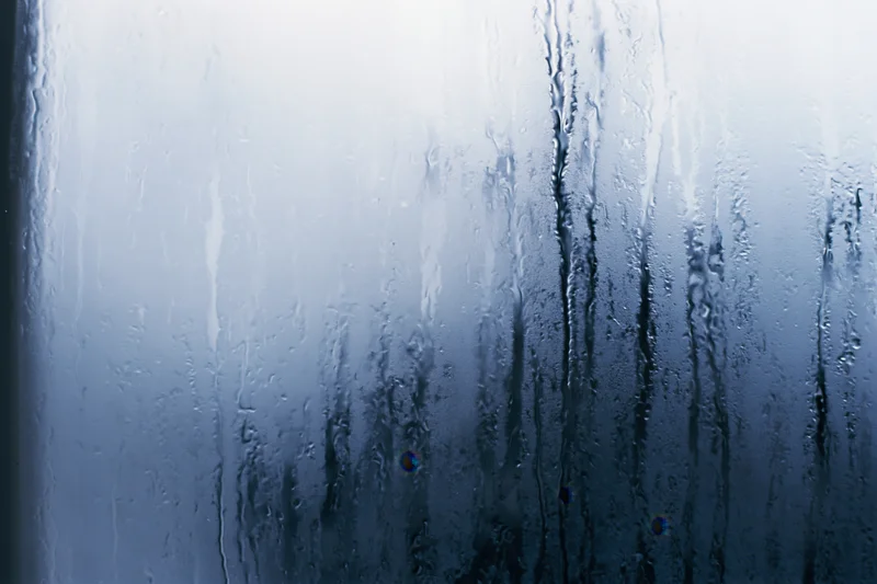 Close-up of fogged glass window with condensation streaks and water droplets